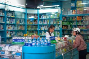 Lokale apotheek in Vietnam met een medewerker in witte jas achter de balie die een klant met motorhelm helpt, omringd door schappen vol medicijnen