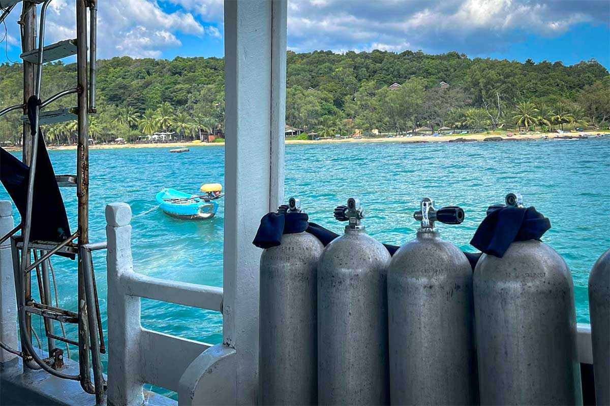 Rij duiktanks op het dek van een duikboot met uitzicht op het turkooizen water en het groene kustlijn van Phu Quoc — dit is het vertrekpunt voor elke duiktrip die vanuit Phu Quoc naar de eilanden vertrekt