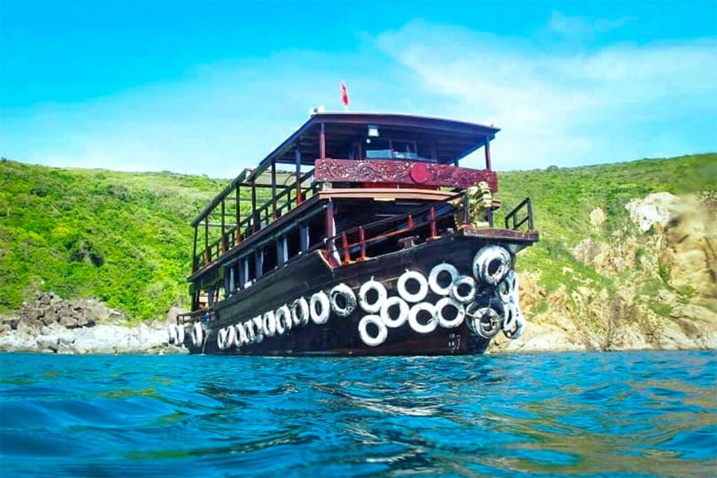 Houten duikboot ankert voor een rotsachtig eiland bij Nha Trang — bootduiken is de standaard manier om de duiklocaties rond Hon Mun en de andere eilanden voor de kust van Nha Trang te bereiken