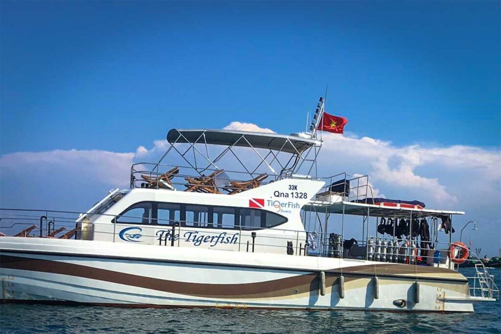 Duikboot The Tigerfish van TigerFish Divers aangemeerd op het water bij Hoi An met duiktanks en wetsuits aan boord — een van de duikboten waarmee dagtrips naar de Cham eilanden vertrekken