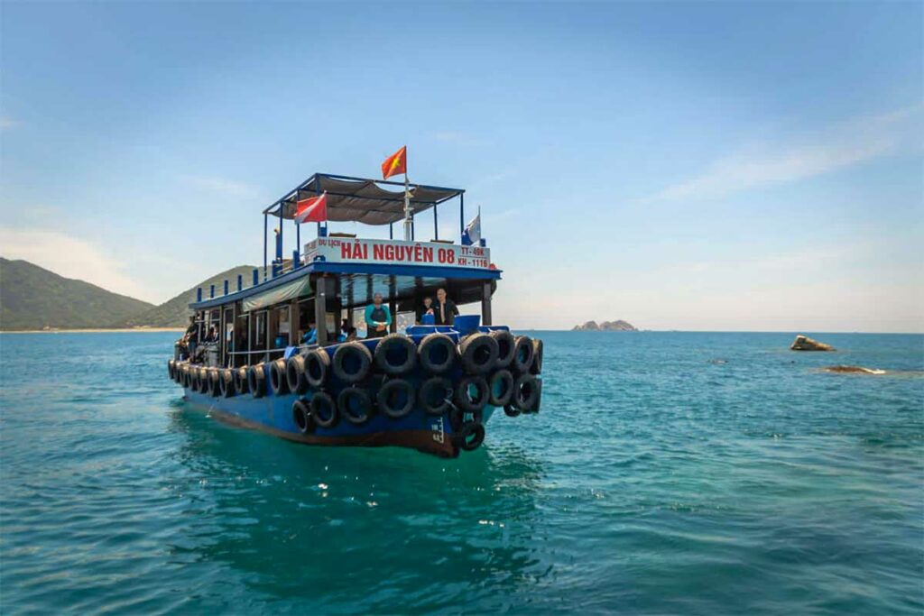 Blauwe duikboot vaart door het heldere water bij de eilanden voor Nha Trang met de duikvlag zichtbaar aan boord — Vietnam Active is een van de duikoperators die dagtrips verzorgt vanuit Nha Trang