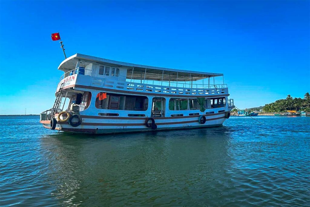Tweedekse duikboot van Vietnam Active ligt voor anker in de haven van Phu Quoc met palmbomen en een strand op de achtergrond — Vietnam Active organiseert dagelijkse duiktrips naar de beste duiklocaties bij Phu Quoc