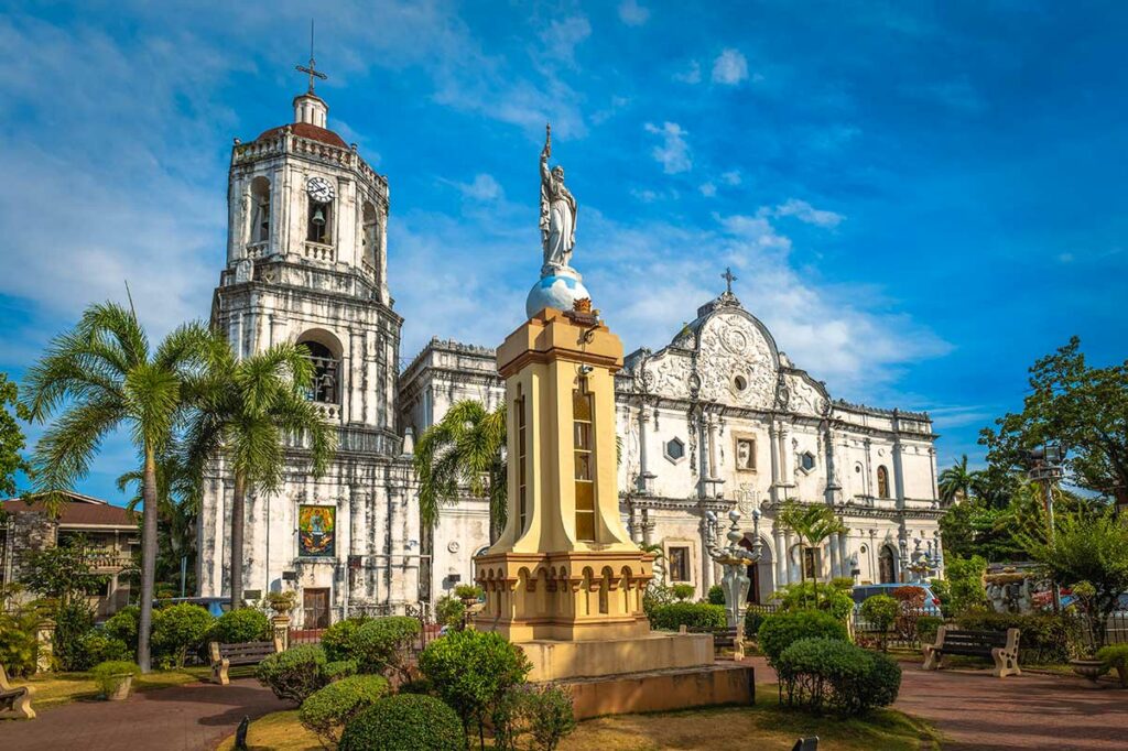 Koloniale Spaans-barokke kathedraal in Cebu op de Filipijnen met een klokkentoren, wit stenen gevel en een standbeeld op een monument ervoor