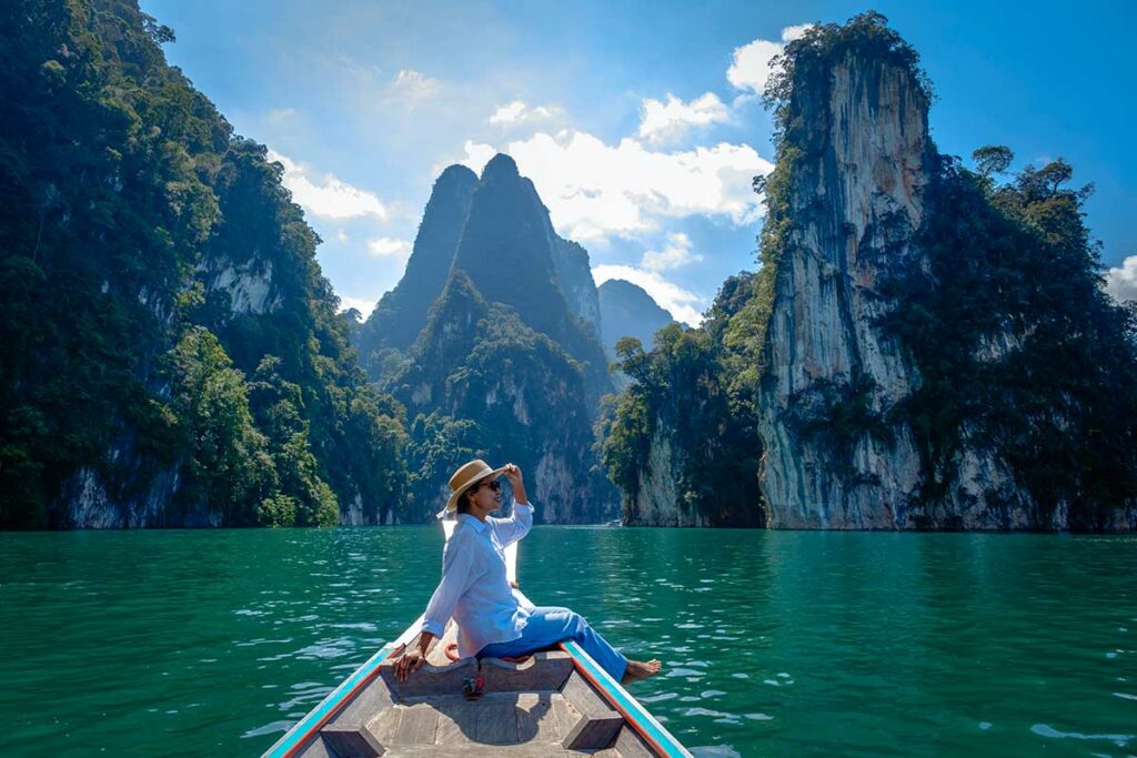Vrouw zit op de boeg van een longtailboot op het groene water van Cheow Lan Lake in Khao Sok National Park, omringd door hoge kalkstenen rotswanden begroeid met tropisch woud
