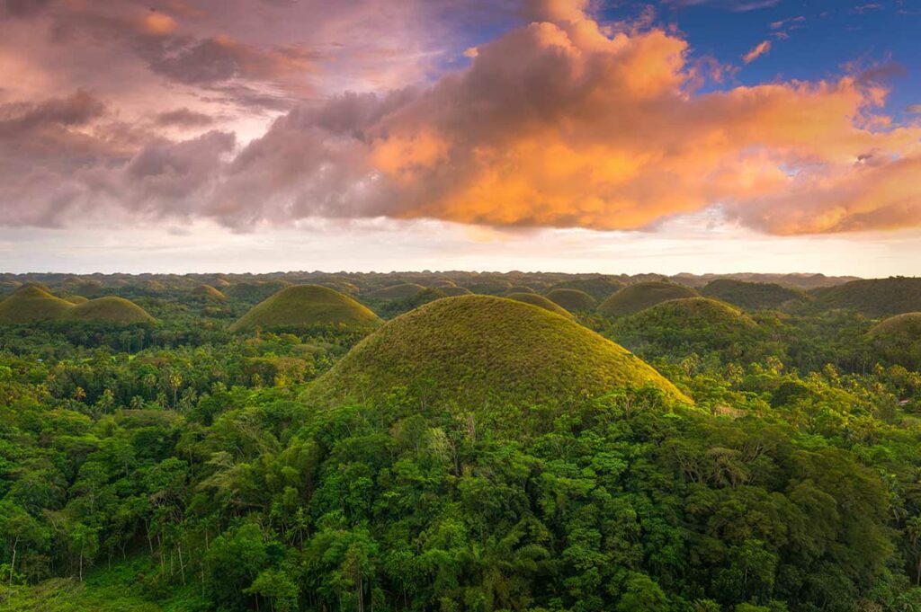 Honderden gelijkmatig gevormde groene heuvels van de Chocolate Hills op Bohol in de Filipijnen, gefotografeerd bij zonsondergang met oranje wolken boven het landschap