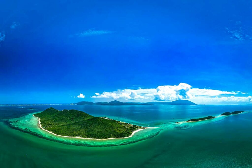 Panoramisch luchtfoto van de drie eilanden van Diep Son in de Van Phong Bay, omgeven door helderblauw en turquoise water met koraalriffen zichtbaar onder het oppervlak en bergen aan de horizon