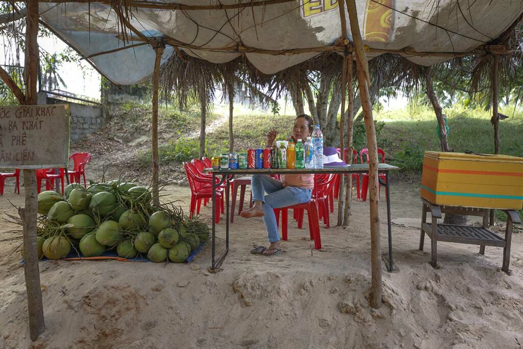 Vietnamese vrouw verkoopt drankjes en kokosnoten onder een rieten afdak aan het begin van de Fairy Stream in Mui Ne