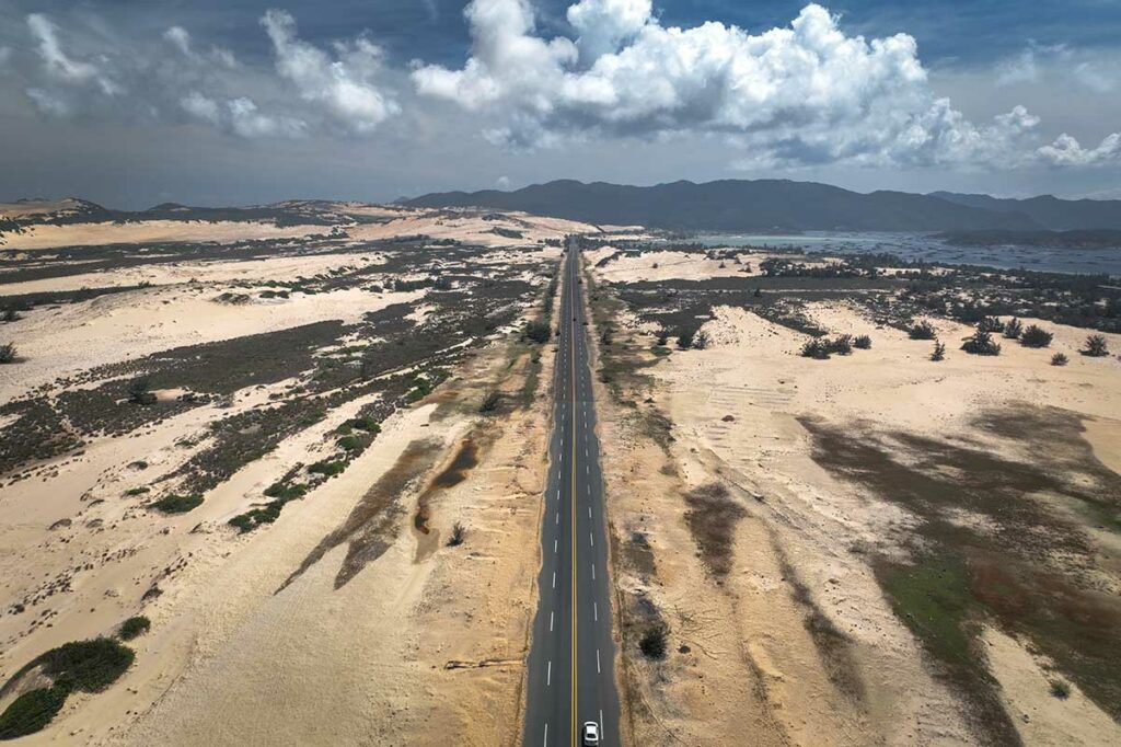 Rechte weg door de kale zandduinen van de Van Phong Bay met aan de horizon de baai en bergen zichtbaar — een onverwacht woestijnachtig landschap aan de kust van centraal Vietnam