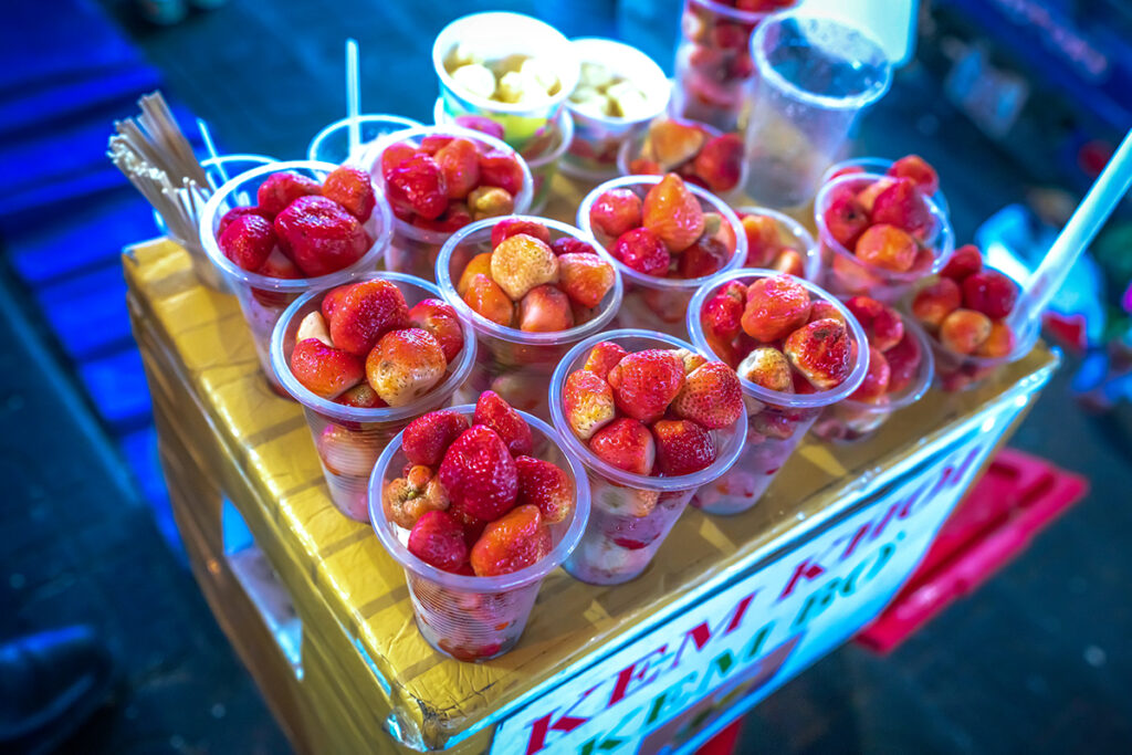 Rij plastic wegwerpbekertjes met aardbeien bij een straatkraam in Vietnam, een voorbeeld van het overmatige plasticgebruik waarmee duurzame reizigers in Vietnam rekening houden