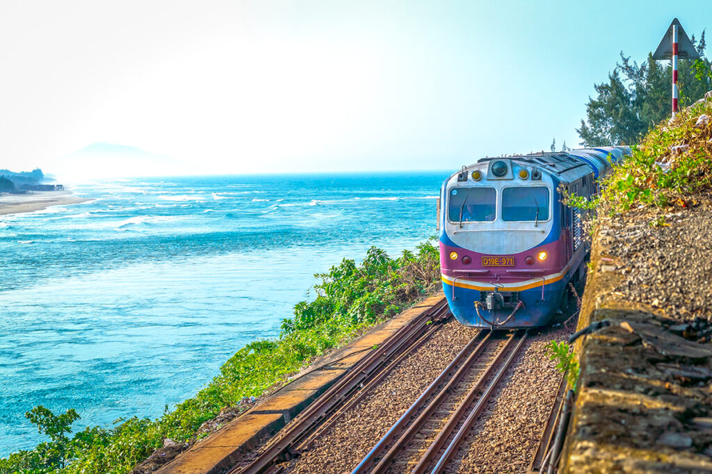 Vietnamese trein rijdt langs de kustlijn met turquoise zee op de achtergrond, de trein is een van de duurzaamste en meest verantwoorde manieren om door Vietnam te reizen