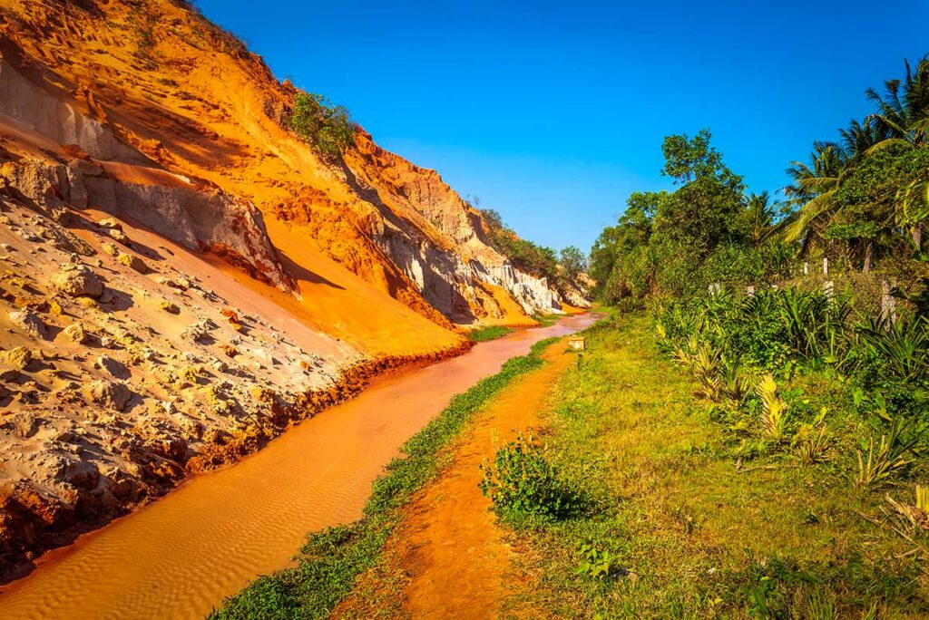 Rood en oranje gekleurd stroombed van de Fairy Stream in Mui Ne met een kleurrijke zandsteen canyon en weelderig groen aan de rechterkant