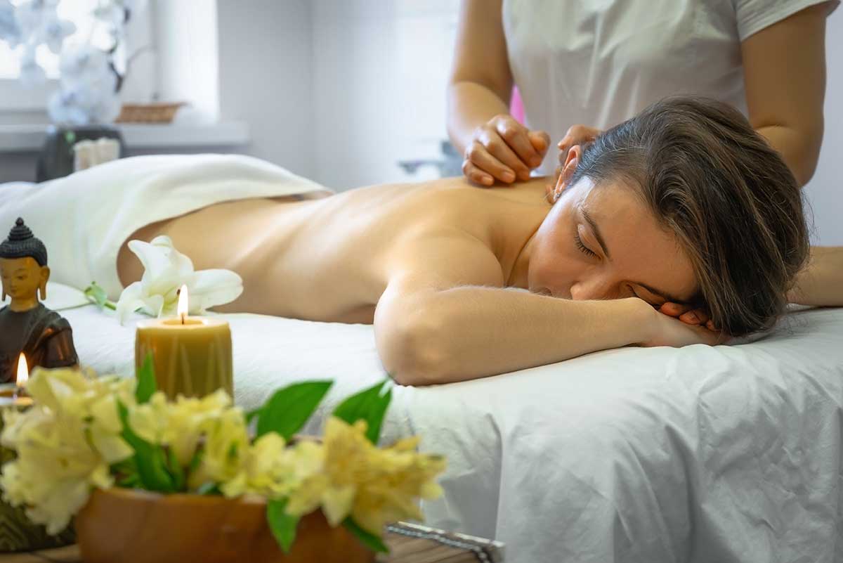 Vrouw ontvangt een full body massage op een witte massagetafel in Vietnam, met kaarsen en bloemen op de voorgrond