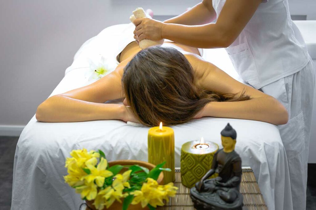 Vrouw ontvangt een full body massage met kruidenstempel op haar rug in een Vietnamese spa, met kaarsen en een Boeddhabeeld op de voorgrond