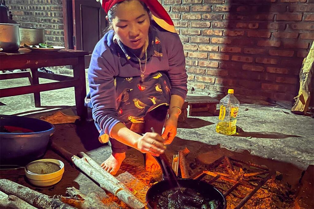 Vrouw van een etnische minderheid bereidt het avondeten op een open vuur in de keuken van een homestay in Sapa, een authentieke ervaring die reizigers in een Vietnamese gastfamilie kunnen meemaken