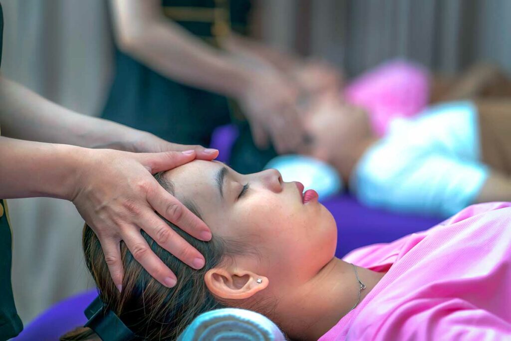 Vietnamese therapeut geeft een hoofdmassage aan een vrouw in een massagesalon in Vietnam, met een tweede klant zichtbaar op de achtergrond