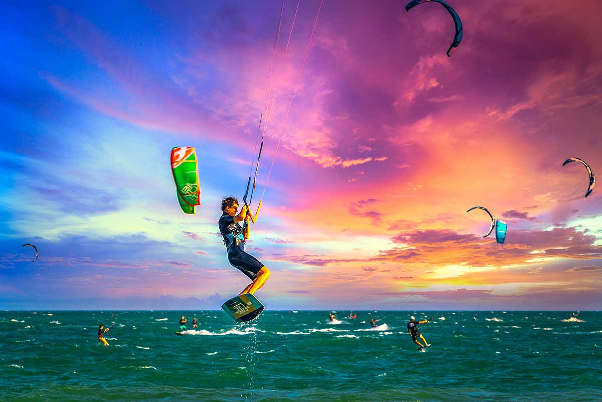 Kitesurfer maakt een hoge sprong boven het water in Mui Ne bij een kleurrijke zonsonderganglucht met meerdere surfers op de achtergrond