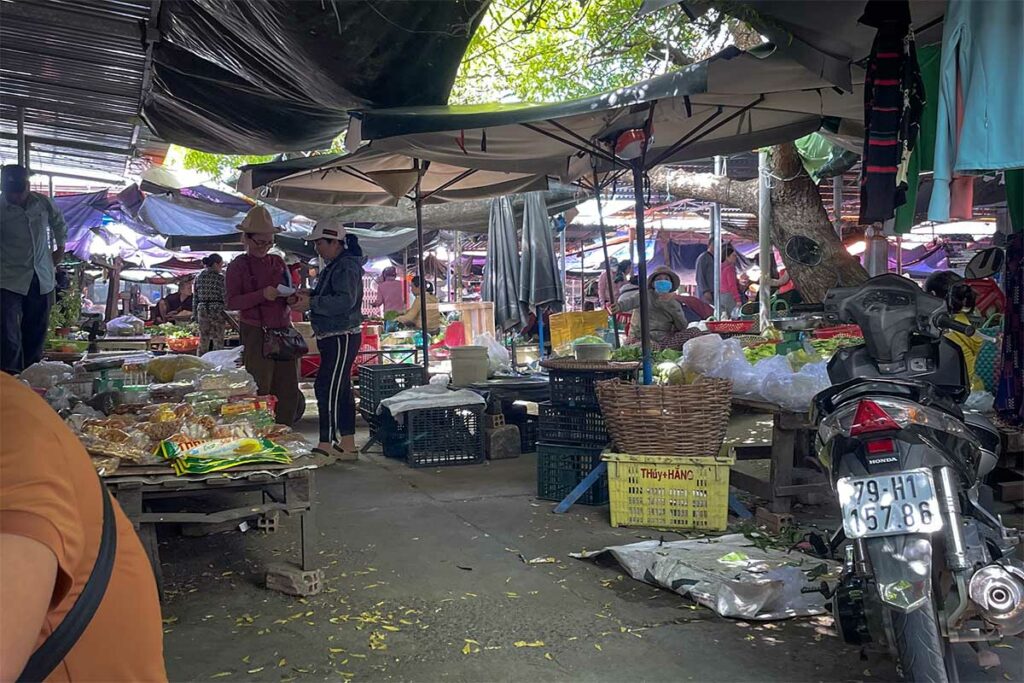 Lokale markthandelaren met groenten, snacks en etenswaren op de buitenmarkt van Ninh Thuy bij Doc Let — een authentieke plek waar lokale bewoners dagelijks boodschappen doen