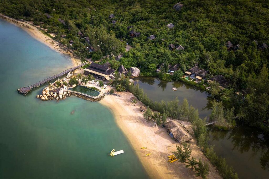 Luchtfoto van het Lalya resort in Ninh Van Bay met rieten bungalows verspreid in de jungle, een zwembad naast de rotsen, een zandstrand en gele kajaks klaar voor gebruik