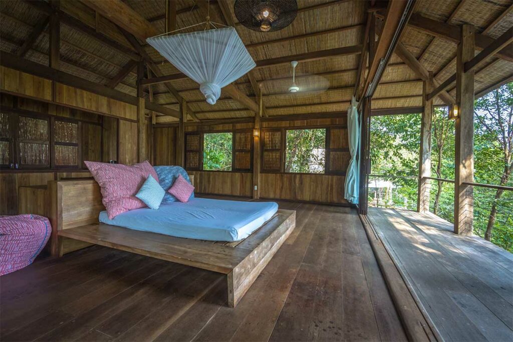 Houten bungalow op Phu Quoc met een klamboe boven het bed en uitzicht op het groene regenwoud — een effectieve bescherming tegen muggen in Vietnam