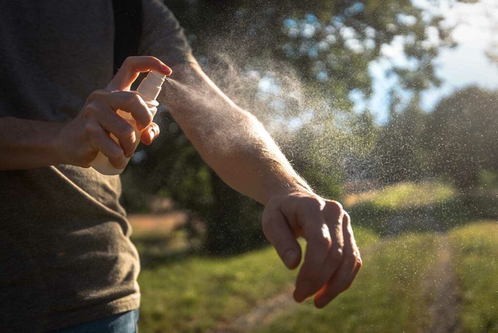 Persoon sproeit insectenwerend middel op de onderarm bij zonsondergang buiten — een van de meest effectieve manieren om dengue te voorkomen in Vietnam