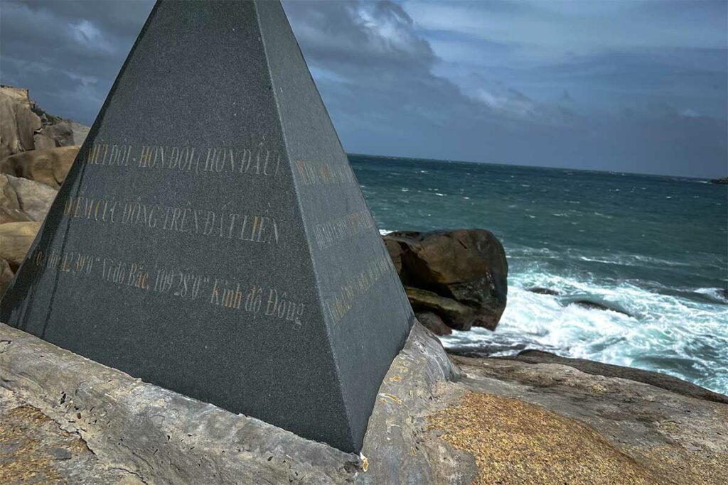 Granieten gedenksteen op Mui Doi met Vietnamese inscriptie die dit aanwijst als het meest oostelijke punt van het Vietnamese vasteland, met ruwe zee op de achtergrond