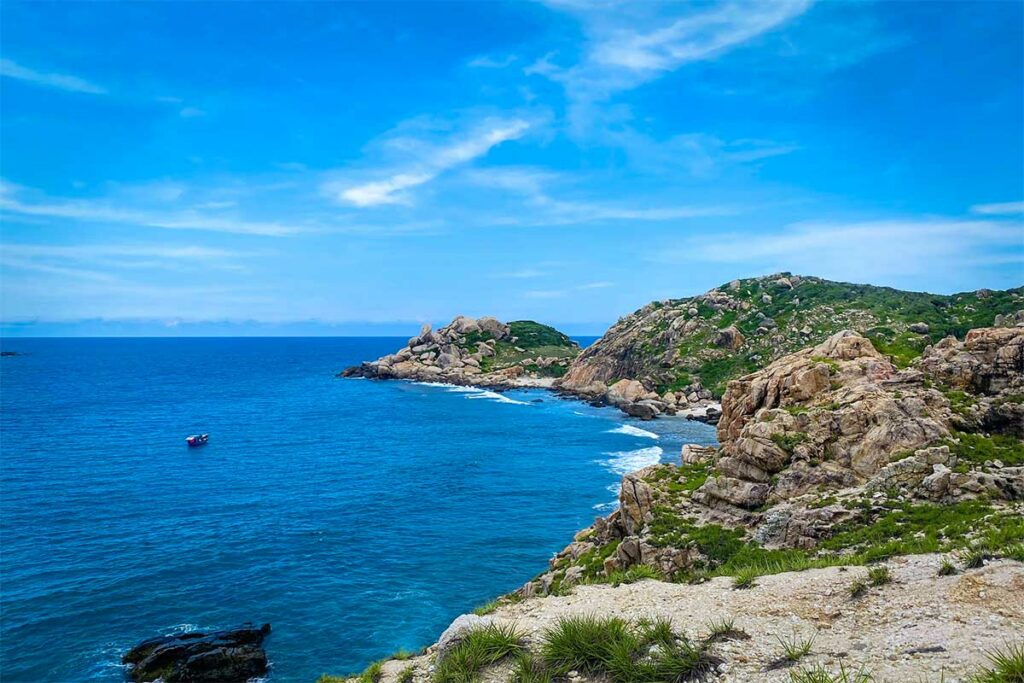 Rotsachtige kustlijn van Mui Doi in de Van Phong Bay met grillige granieten rotsen, groen begroeid land en diepblauw water — een van de meest ongerepte punten van de baai