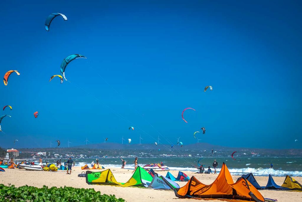 Druk kitesurfstrand in Mui Ne met tientallen kleurrijke vliegers in de lucht en uitgerolde kites op het zand — Mui Ne is een van de beste bestemmingen voor kitesurfen in Vietnam