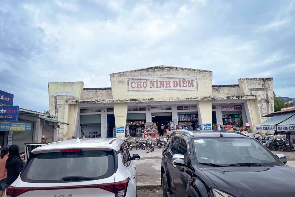 Buitenaanzicht van de Cho Ninh Diem markt in Ninh Thuy bij Doc Let Beach, een lokale markt met een oud betonnen marktgebouw en drukte voor de ingang