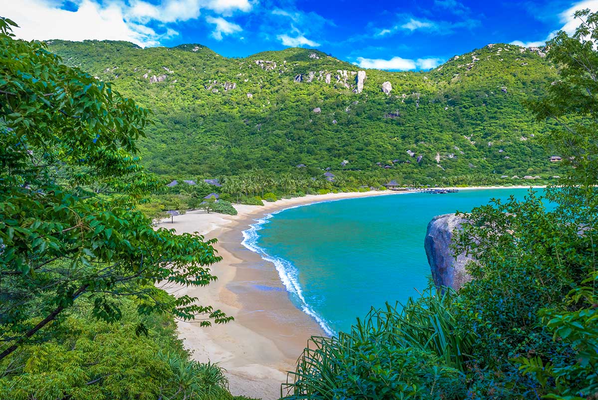 Uitzicht vanuit de jungle op de baai van Ninh Van met een lang wit strand, turquoise water en rieten bungalows van een resort geïntegreerd in de groene berghellingen