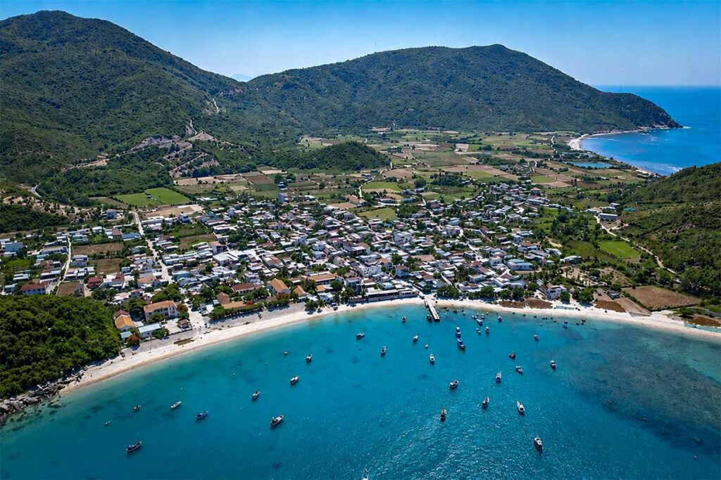 Luchtfoto van het vissersdorp aan de kust van Ninh Van Bay met witte huizen, visserboten in het turkooizen water en groene bergen op de achtergrond — het dorp is alleen per boot bereikbaar