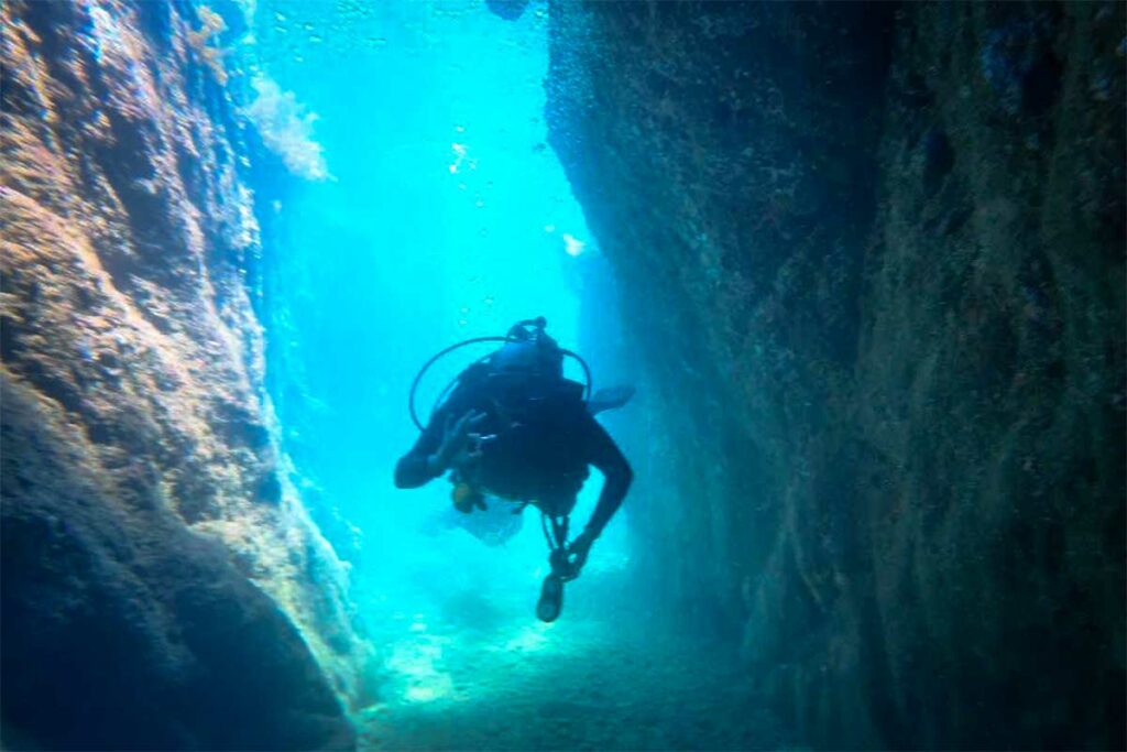Scubaduiker zwemt door een smalle onderwater canyon met blauwe rotswanden bij Nha Trang — de canyon bij Hon Mun is een van de interessantste duiklocaties voor gevorderde duikers in de regio