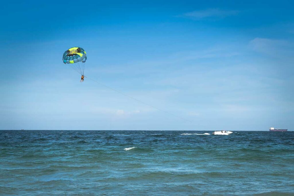 Parasailer hangt hoog boven de zee bij Doc Let Beach aan een kleurrijke parachute, met een speedboot zichtbaar op het water — parasailing is een van de watersportactiviteiten bij Doc Let