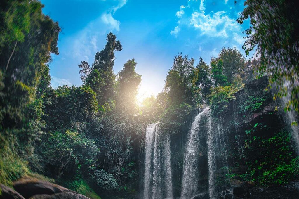Waterval in het junglegebied van Phnom Kulen in Cambodja, fotografeerd vanuit het water met zonlicht dat door de boomtoppen breekt