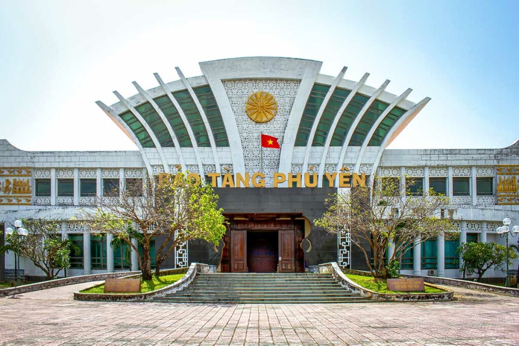 Vooraanzicht van het Phu Yen Museum in Tuy Hoa met een opvallend waaiervorming dak, Vietnamese vlag en brede trappen aan de ingang — het museum biedt informatie over de geschiedenis en cultuur van de provincie