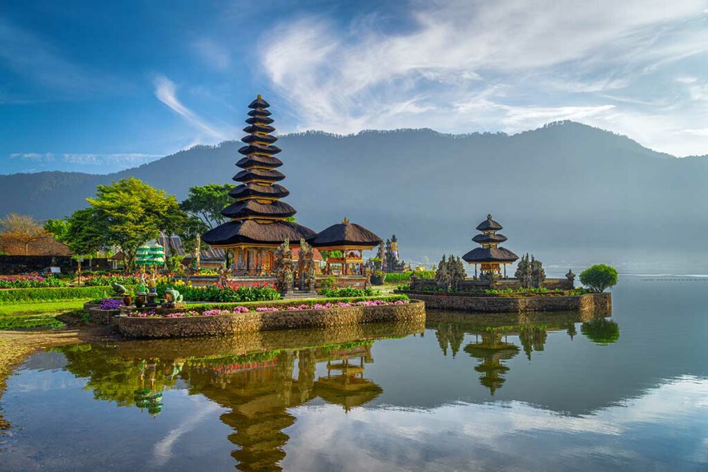 De Pura Ulun Danu Bratan watертempel op Bali weerspiegeld in het rustige meerwater, omgeven door bloemen en bergen in de mist