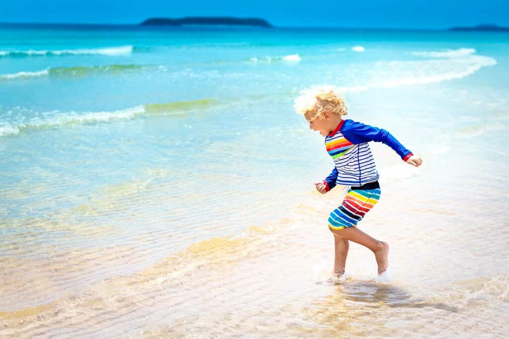 Kind in een kleurrijke rashguard rent door het ondiepe water op een strand in Vietnam, beschermd tegen kwallen en de sterke zon