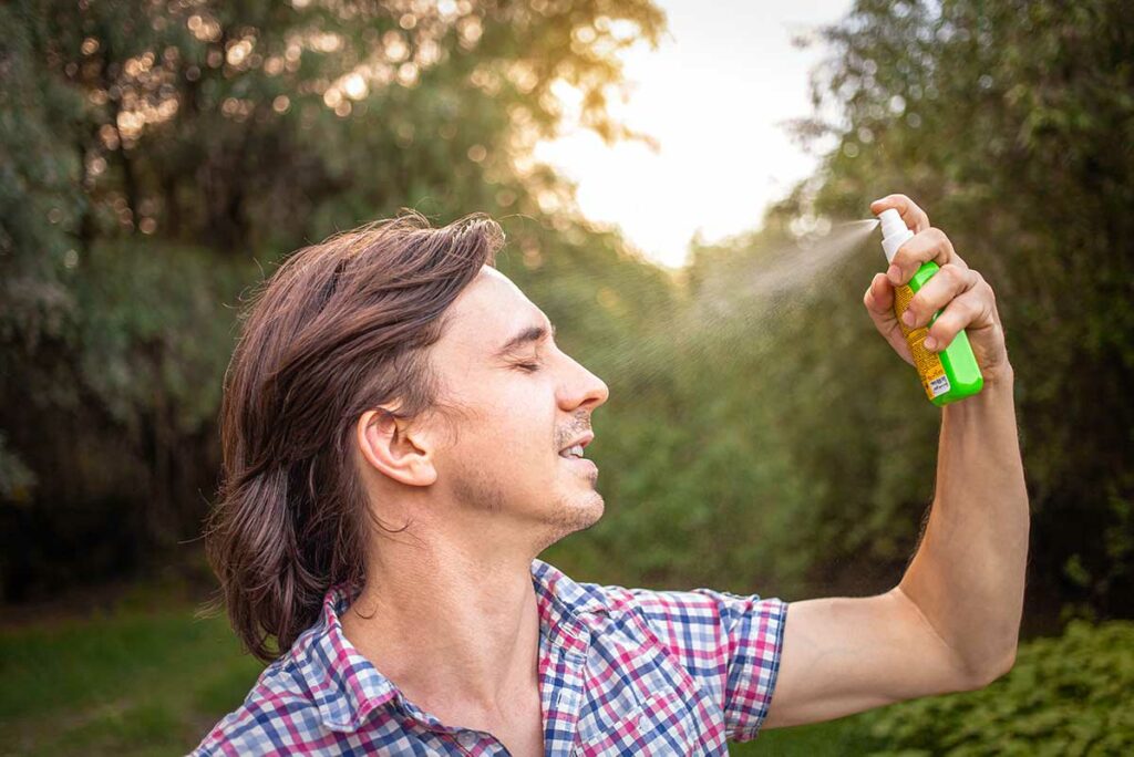 Man sproeit muggenspray op zijn gezicht in een groene buitenomgeving — een essentiële voorzorgsmaatregel tegen muggen in Vietnam