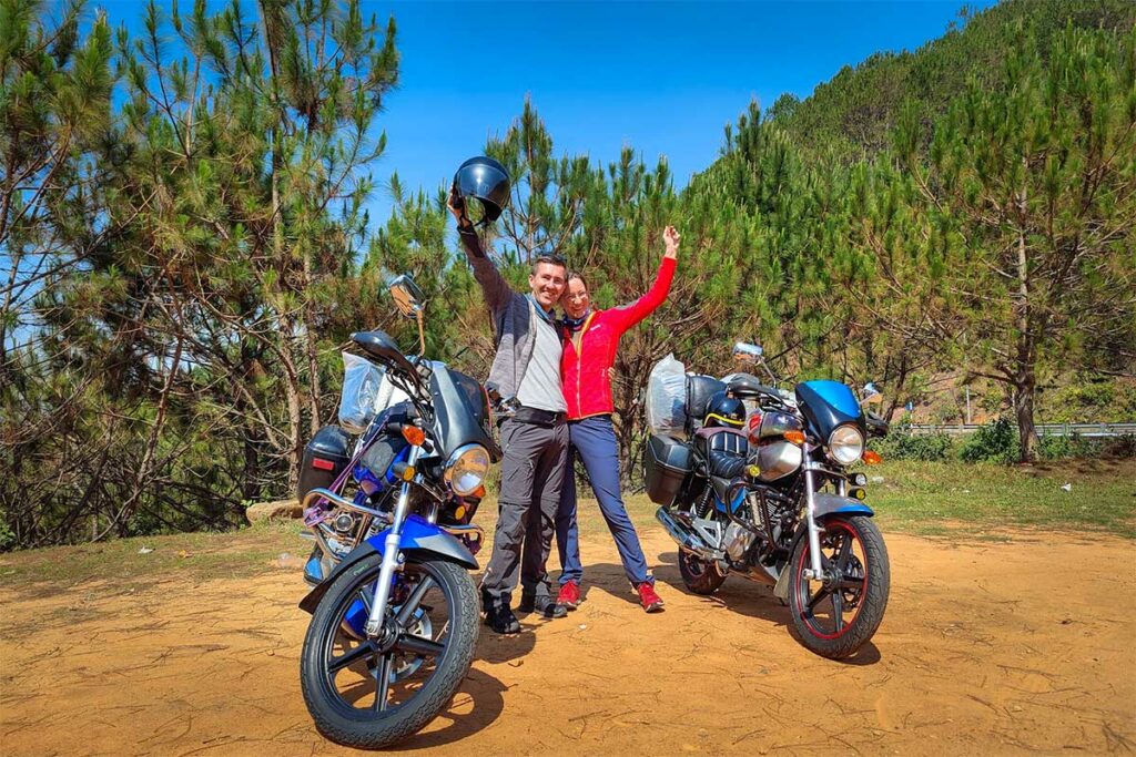 Stel poseert juichend naast twee Easy Rider-motoren bij een dennenbosje buiten Dalat — een Easy Rider tour is een populaire manier om het berglandschap en de omgeving van Dalat te verkennen