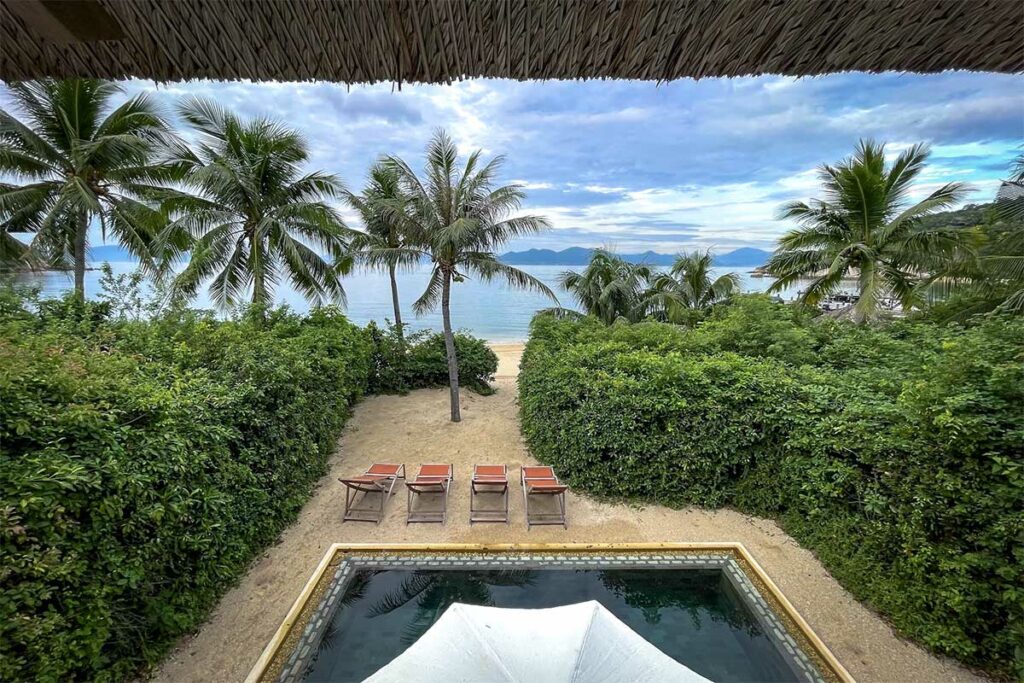 Uitzicht vanuit een villa van Six Senses Ninh Van Bay over een privézwembad, ligbedden, palmbomen en de rustige baai op de achtergrond — een van de meest exclusieve resorts bij Nha Trang