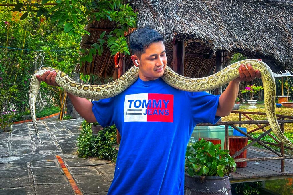 Toerist houdt een grote python vast bij de ingang van de Fairy Stream in Mui Ne — een van de toeristische activiteiten langs het parcours die je kunt overslaan