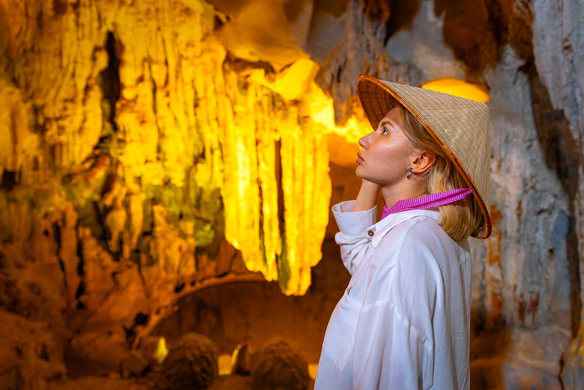 Westerse toerist met Vietnamese conische hoed bewondert de stalactieten in een verlichte grot in Vietnam, verantwoord reizen betekent ook het respecteren van natuurlijke en culturele bezienswaardigheden