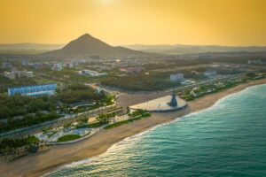 Luchtfoto van de kustlijn van Tuy Hoa bij zonsondergang met de Nghinh Phong toren op het strand, een lang strandplein, gebouwen van de stad en een conische berg op de achtergrond