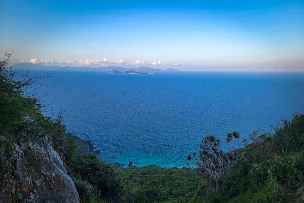 Wijd zeezicht vanaf het uitzichtpunt op het Hon Heo schiereiland in de Van Phong Bay, met eilanden zichtbaar aan de horizon en weelderige kustvegetatie op de voorgrond