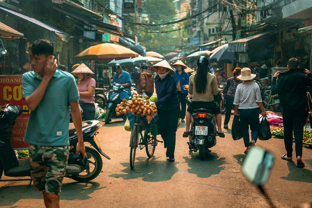 Drukke marktstraat in Vietnam met scooters, fietsers en voetgangers door elkaar, een typisch beeld dat elke reiziger op vakantie in Vietnam tegenkomt
