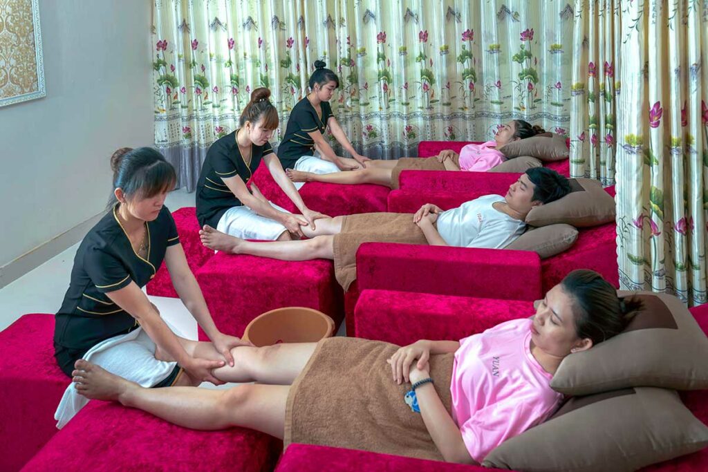 Drie klanten liggen op rode bedden terwijl twee Vietnamese therapeuten een voetmassage geven in een massagesalon in Vietnam