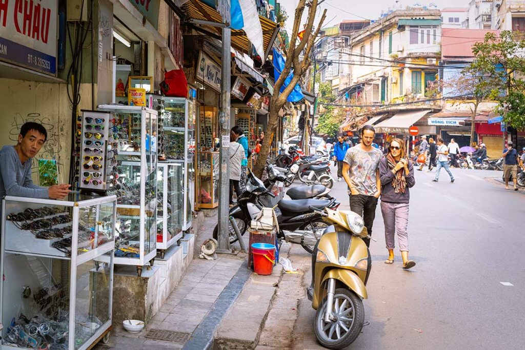 Westerse toeristen lopen langs een straatverkoper met zonnebrillen in de oude binnenstad van Hanoi, Vietnam
