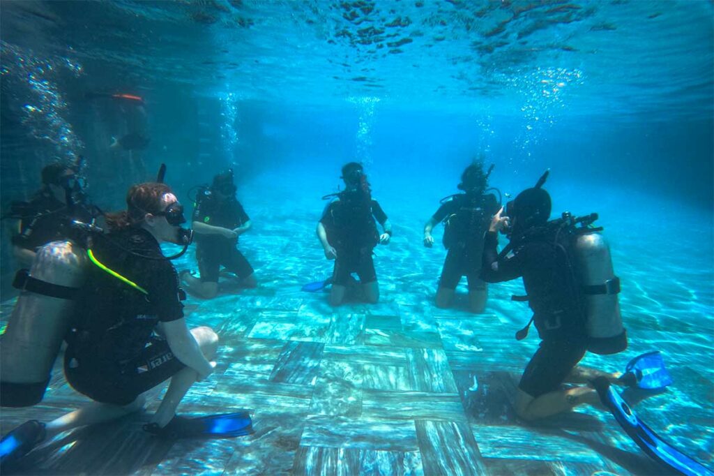 Groep cursisten oefent duikvaardigheden op de bodem van een zwembad tijdens een PADI-duikcursus in Hoi An — zwembadtraining is de eerste stap voor wie leert duiken bij Hoi An
