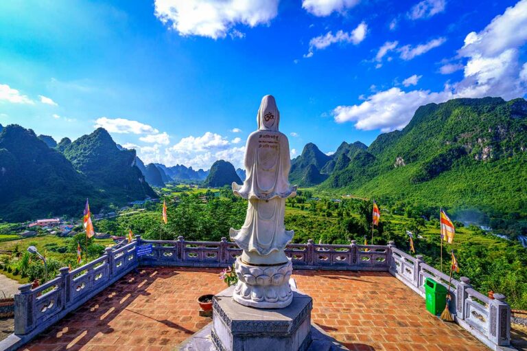 Wit boeddhabeeld op het terras van de Truc Lam pagode met uitzicht over de kalksteenbergen bij Ban Gioc