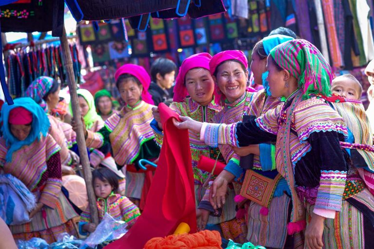 Vrouwen bekijken rode stof bij een textielkraam op de markt van Bac Ha, provincie Lao Cai.