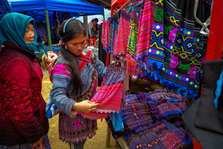 Jonge vrouw met kind op de rug bekijkt geborduurde rokken op de markt van Can Cau.